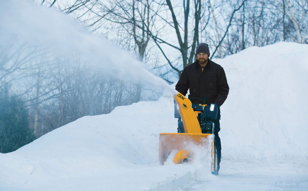 man pushing snow blower through snow covered field