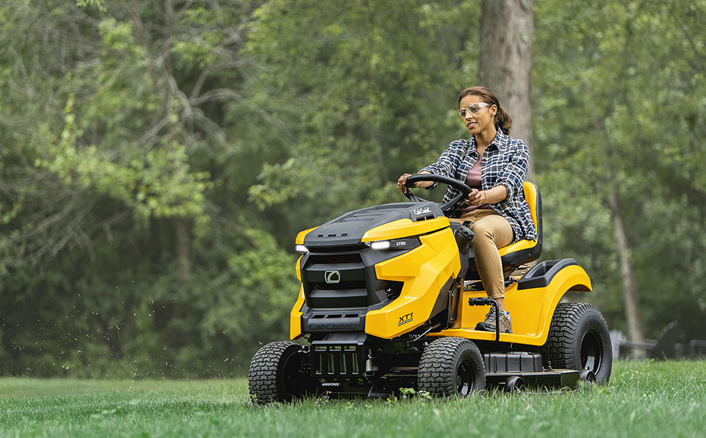 woman riding cub cadet mower through grassy yard