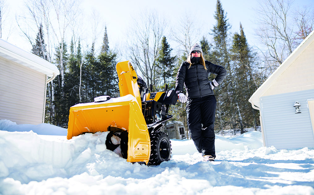 woman standing next to snow blower in snow covered field