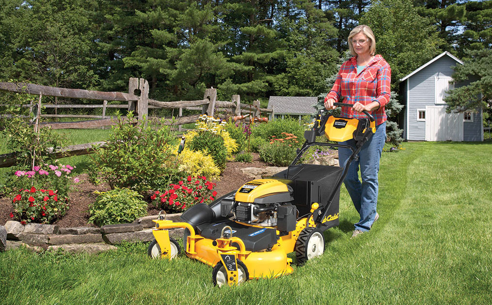 woman mowing in front of her garden bed with a wide-area walk-behind mower