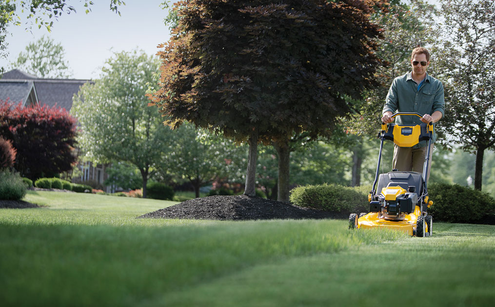 woman mowing in front of her garden bed with a wide-area walk-behind mower